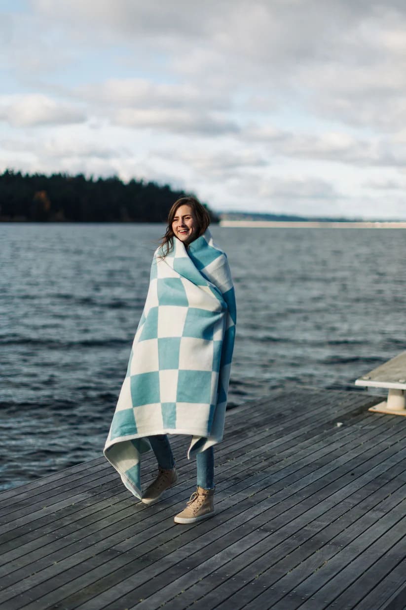 The Westerly Co Boardwalk blanket gives casual coastal vibes. The square checker pattern in white and blue, transport you to the sunlit boardwalk, where the sound of the waves and the ocean breeze await. Wrap up on the dock or anywhere you could use an extra layer.